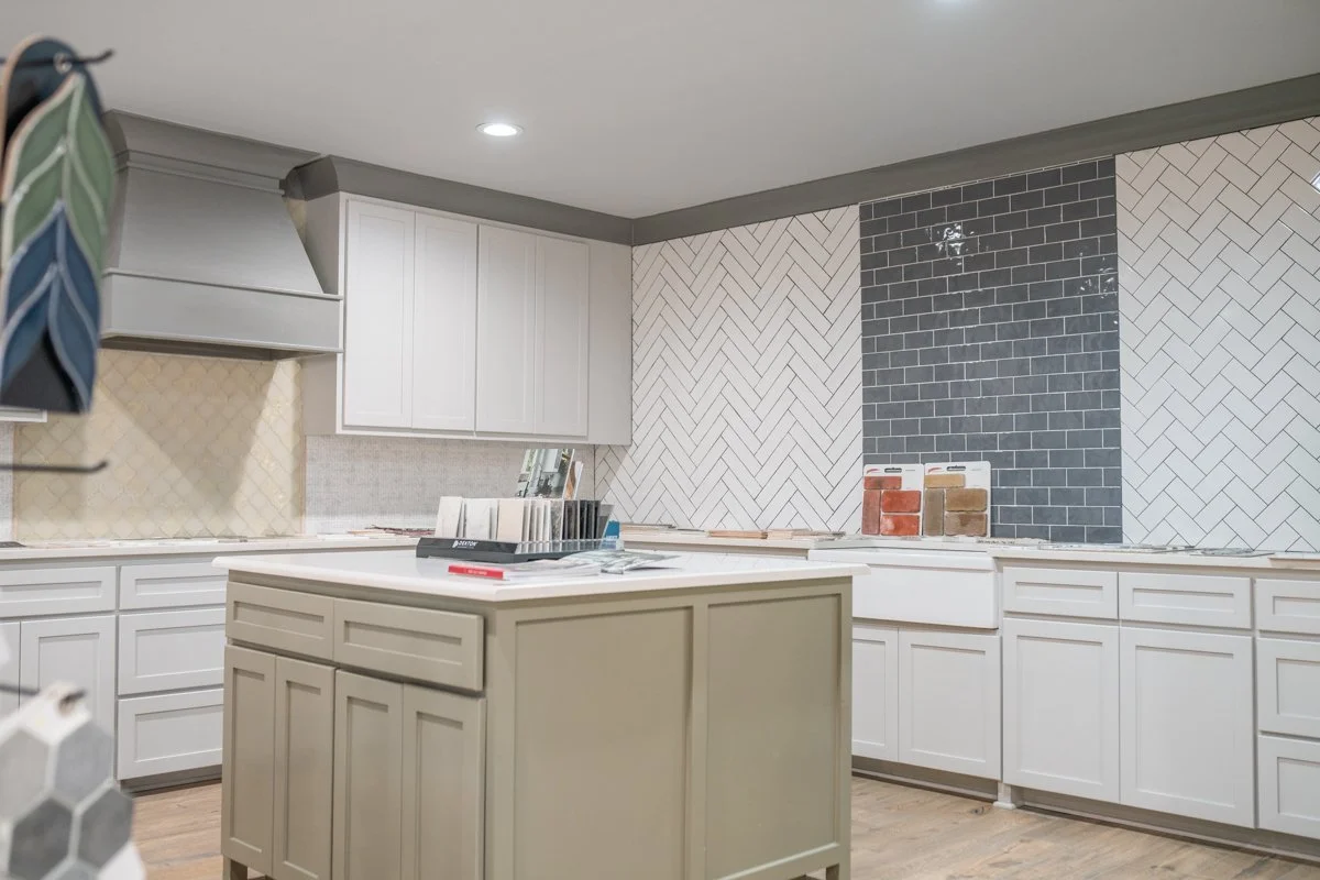 Kitchen with white cabinets, an island, and herringbone tile backsplash in progress, featuring a section of black subway tile and sample tiles on the counter.