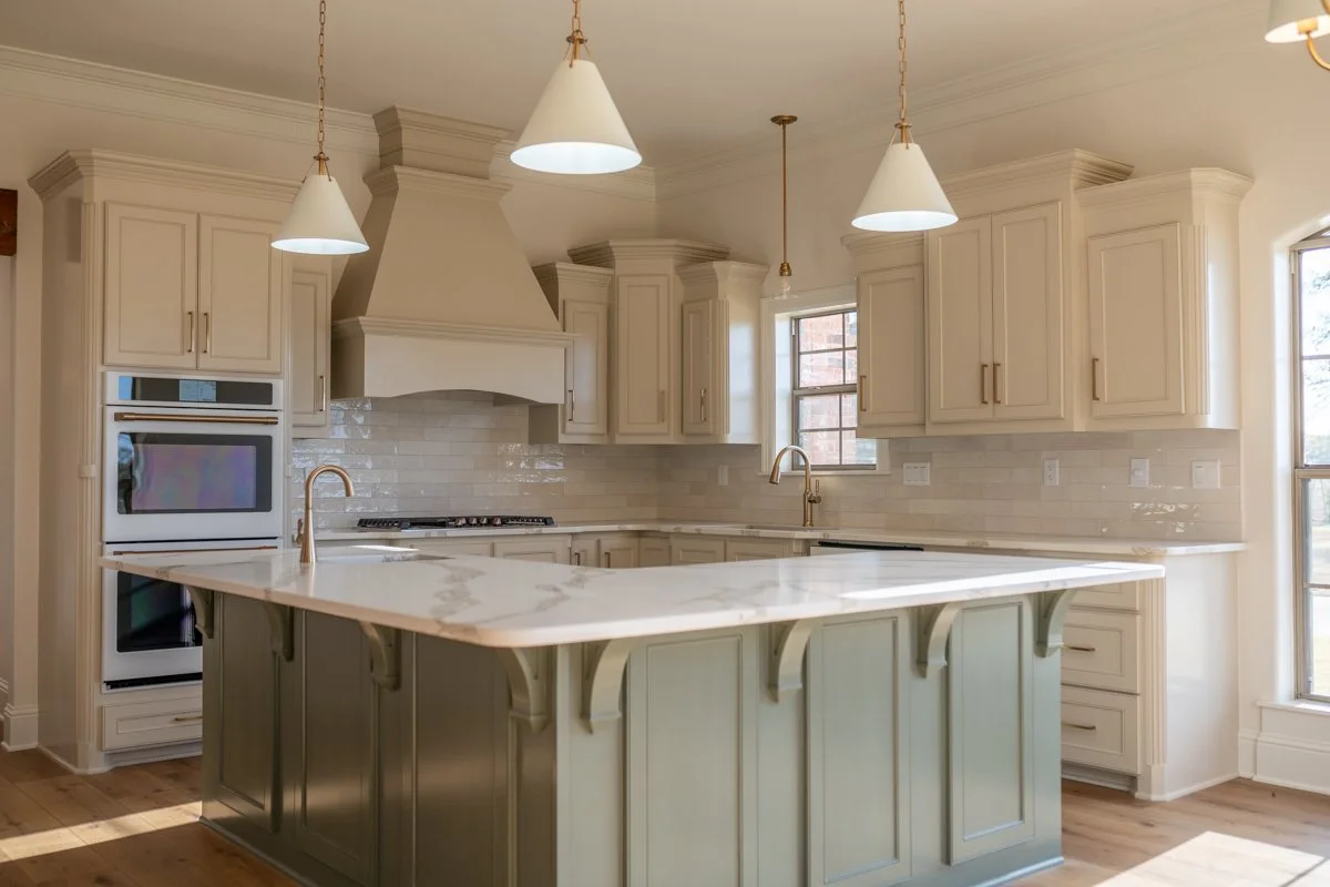 Modern kitchen with white cabinets, marble island, double oven, brass fixtures, and pendant lighting.