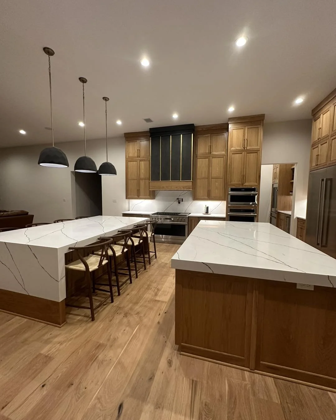 Modern kitchen with wooden cabinetry, a large white marble island, and pendant lighting.