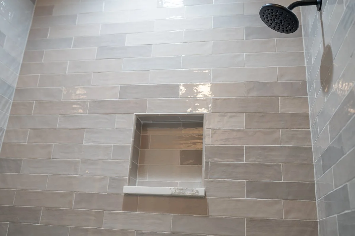 Shower with beige tile walls, a black showerhead in the upper right corner, and a built-in tile niche with a marble shelf.