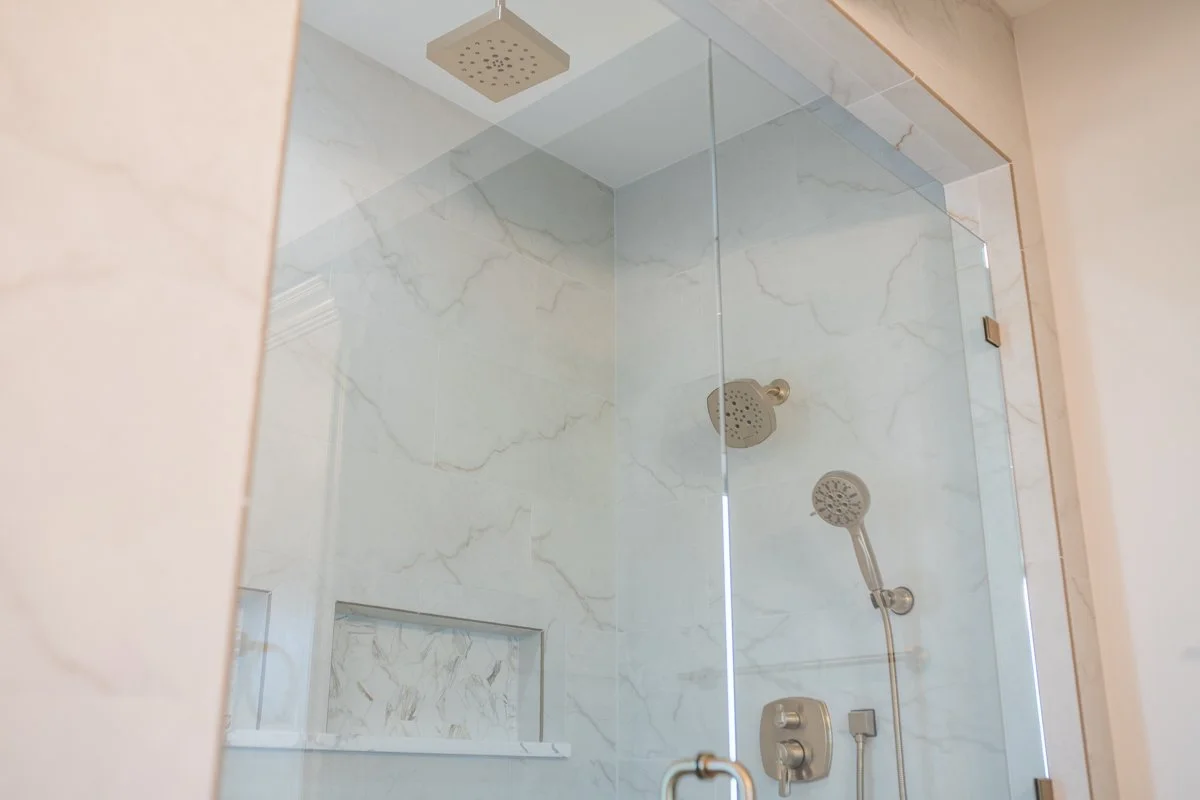 Shower with marble walls, a rain showerhead, a handheld showerhead, and a built-in shower niche