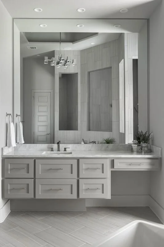 Modern bathroom with a large mirror, white vanity with drawers, tiled walls, and minimal decor.