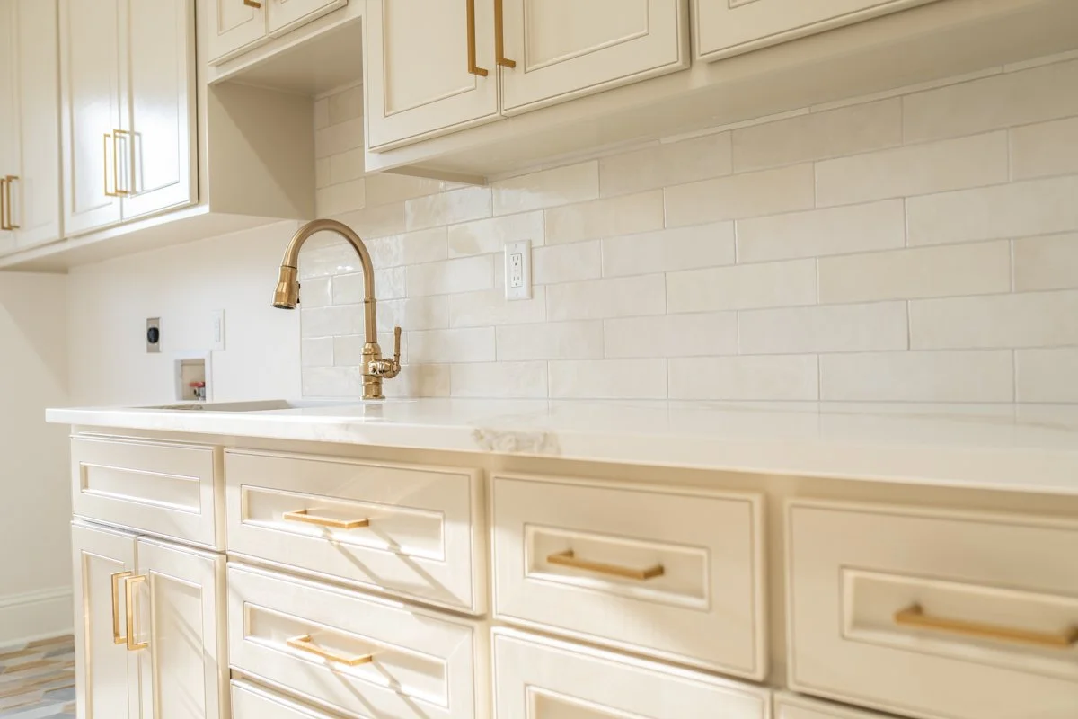 Kitchen with cream-colored cabinets, a marble countertop, and a gold faucet.