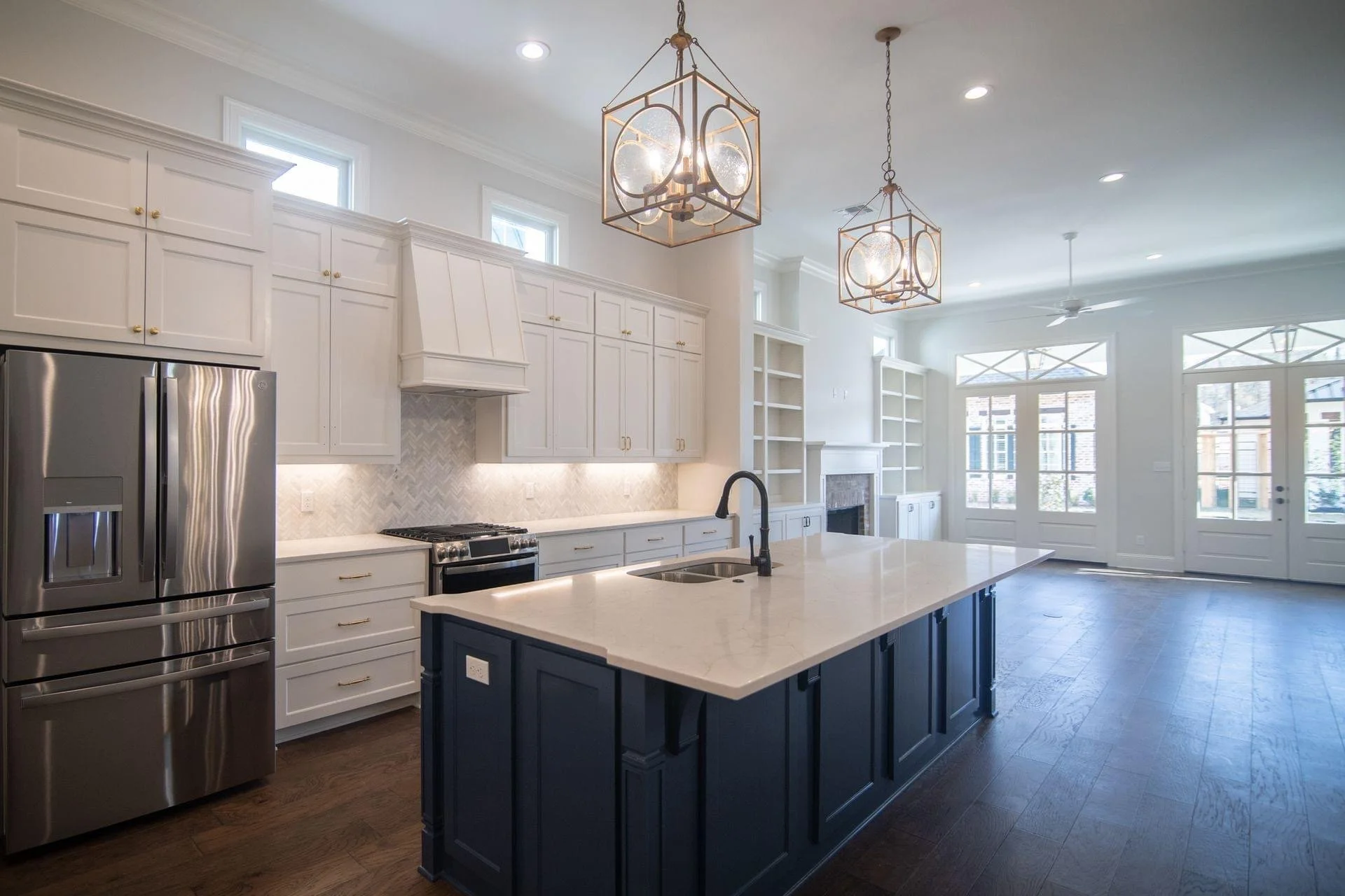 Bright modern kitchen with white cabinets, a dark blue island, stainless steel refrigerator, and large windows.