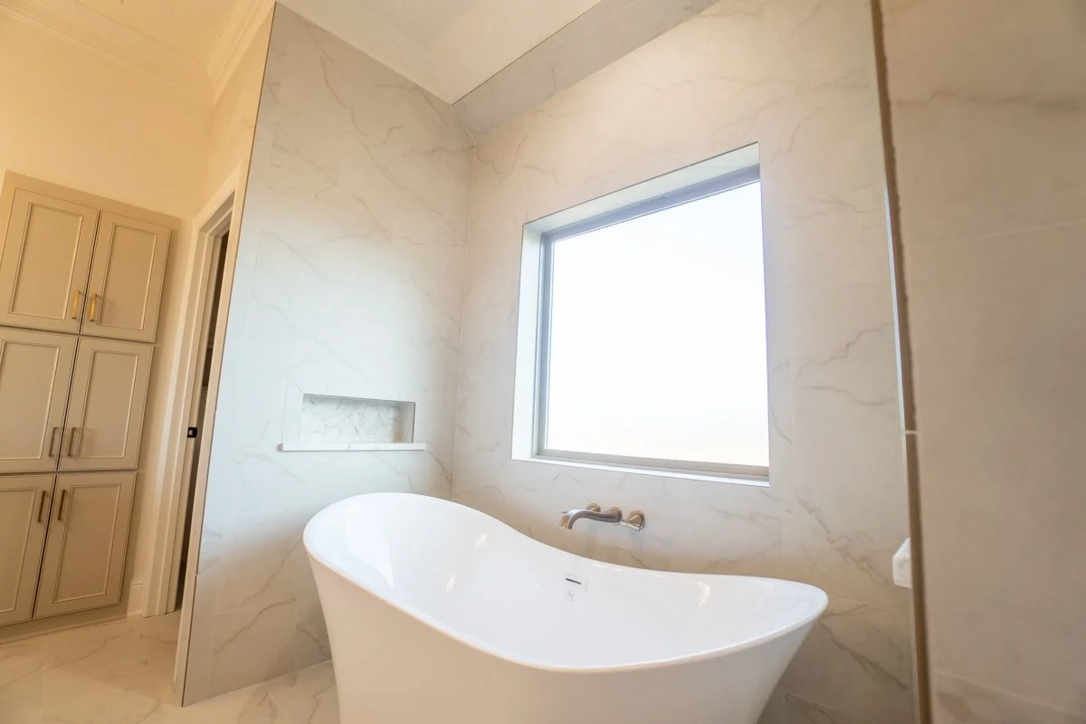 Modern bathroom with a freestanding bathtub, marble walls, a large window, and built-in shelf.