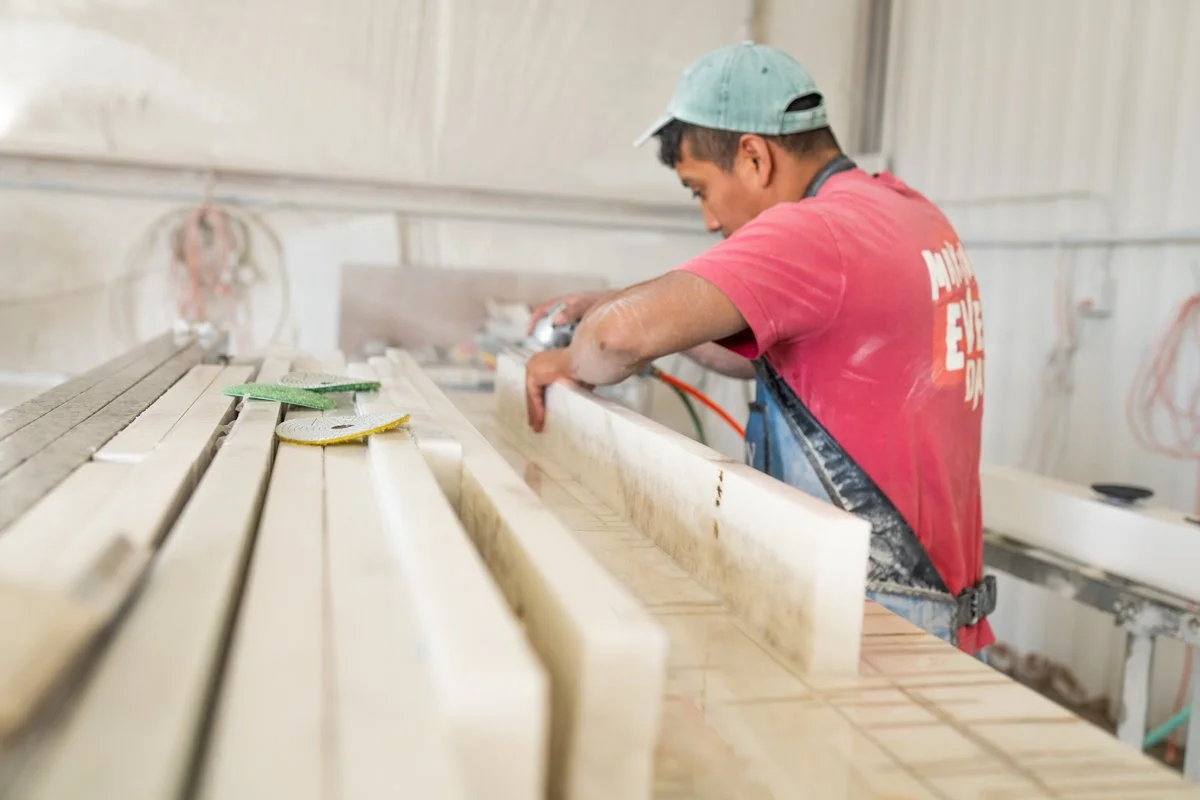 A man in a red shirt and a baseball cap working with wood in a workshop.