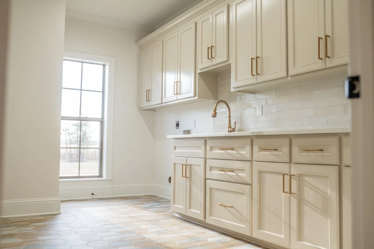 Kitchen with light beige cabinets, a window with natural light, and a white tiled backsplash.