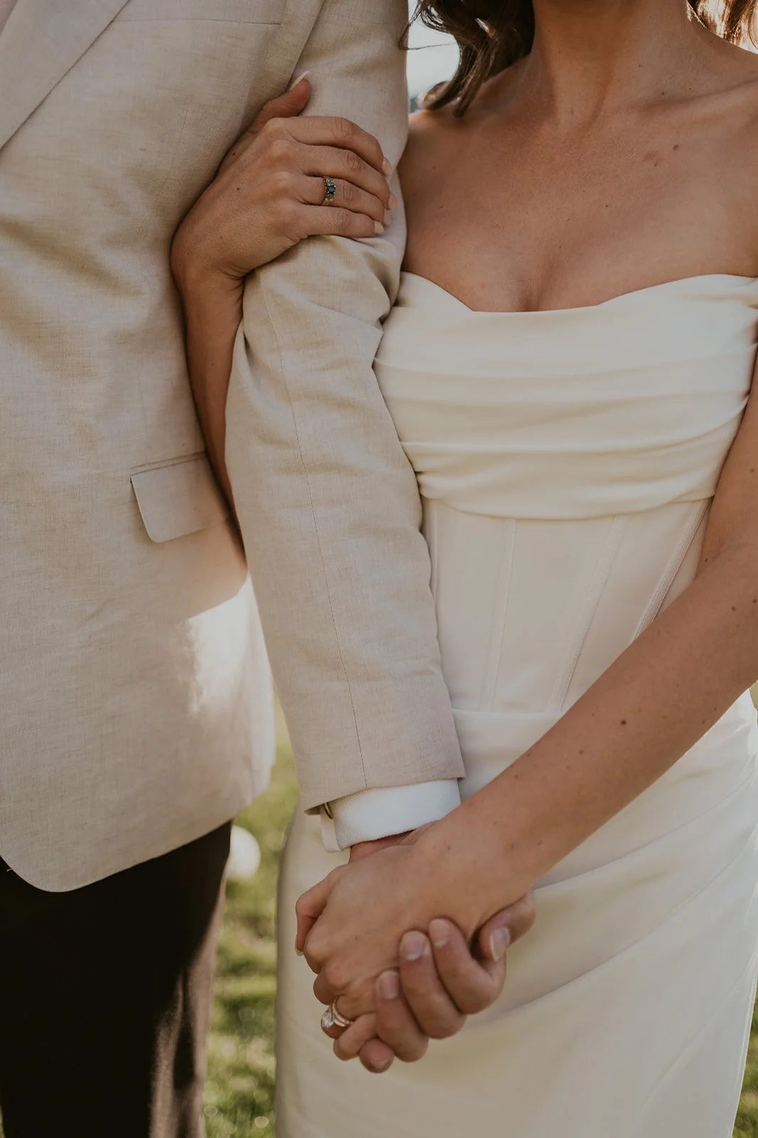 Close-up of a couple holding hands during a wedding, with the woman wearing a white dress and the man in a light-colored suit.