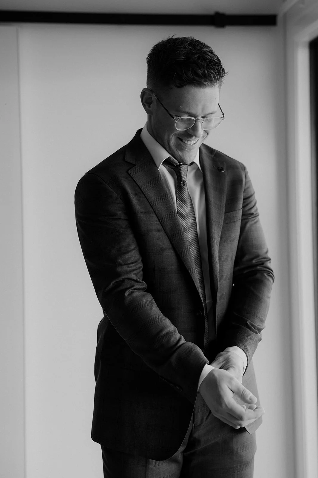A black and white photo of a man in a suit and glasses smiling and getting ready, possibly for a formal event.