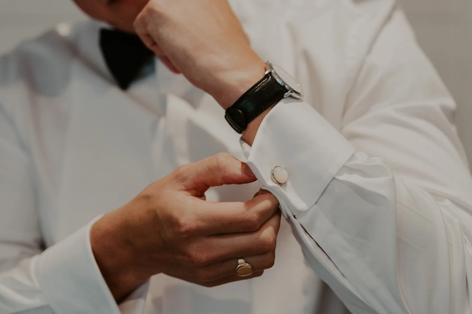 A person in a white dress shirt adjusting a shirt cuff with a cufflink, wearing a black watch.