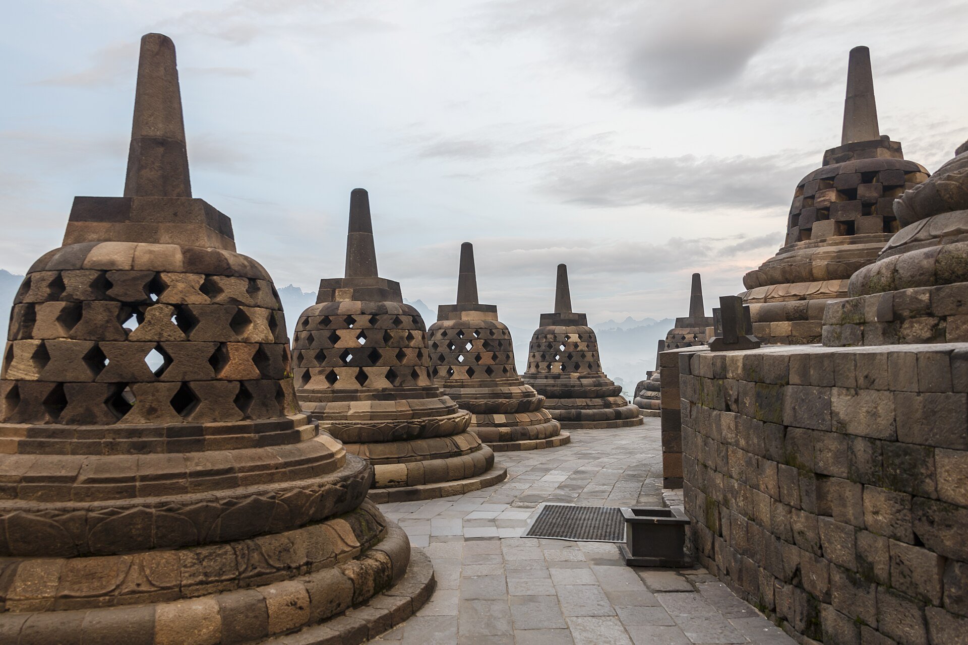 Series of ancient Buddhist stupas called pagodas with rounded bases and conical spires in a cloudy sky setting.
