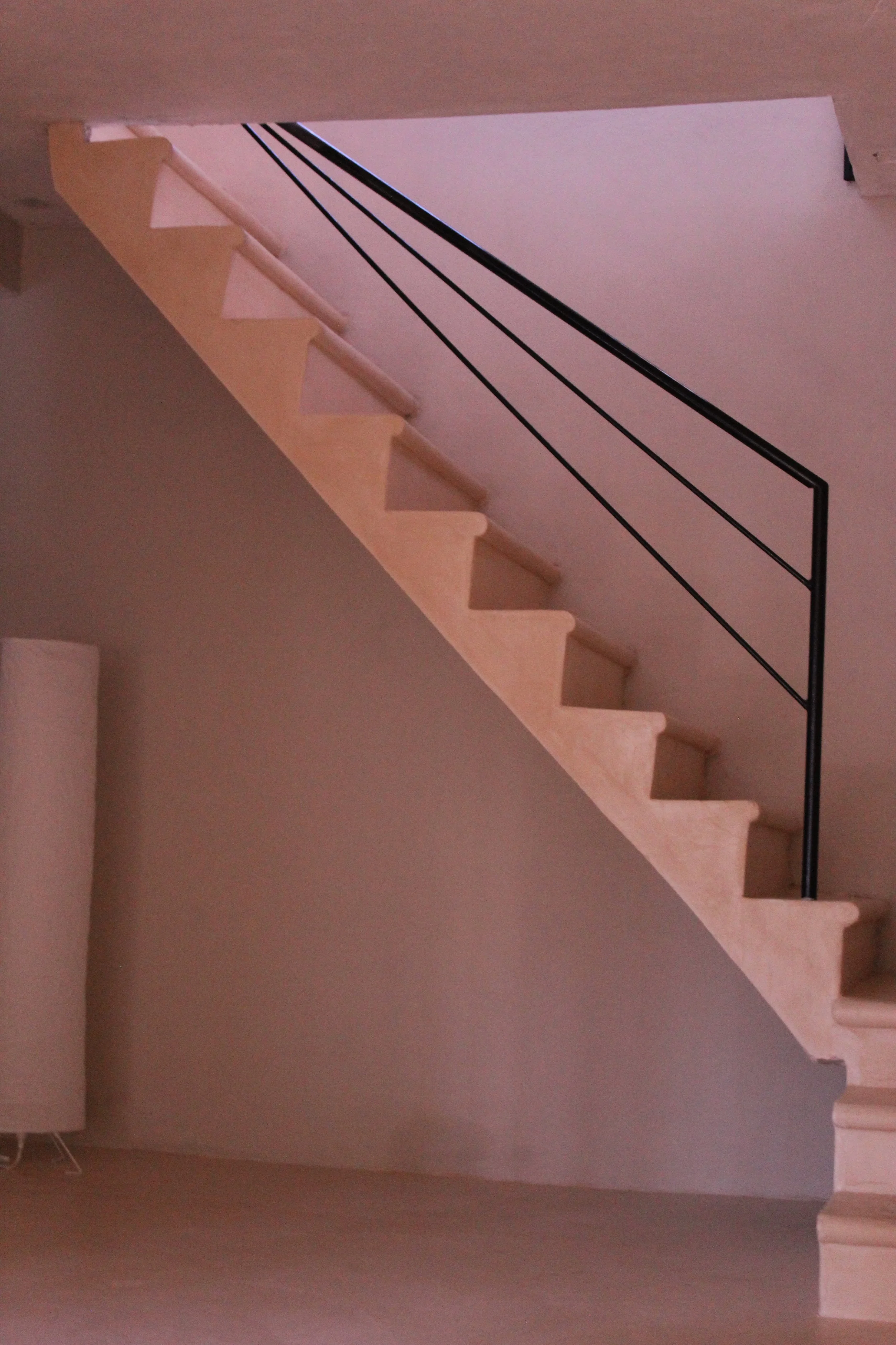 Interior view of a staircase with wooden steps and a black metal railing, leading to an upper floor, with beige walls around.