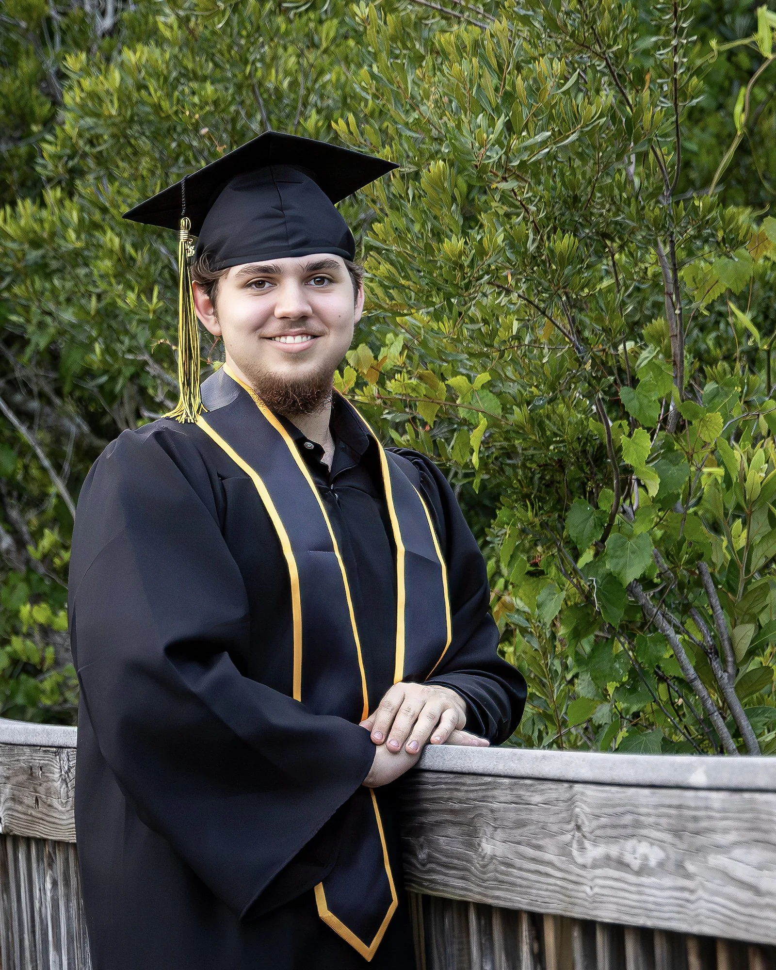 Gulf Breeze senior portrait — high school graduate in cap and gown on a wooden boardwalk, natural light, Barefoot Photography LLC
