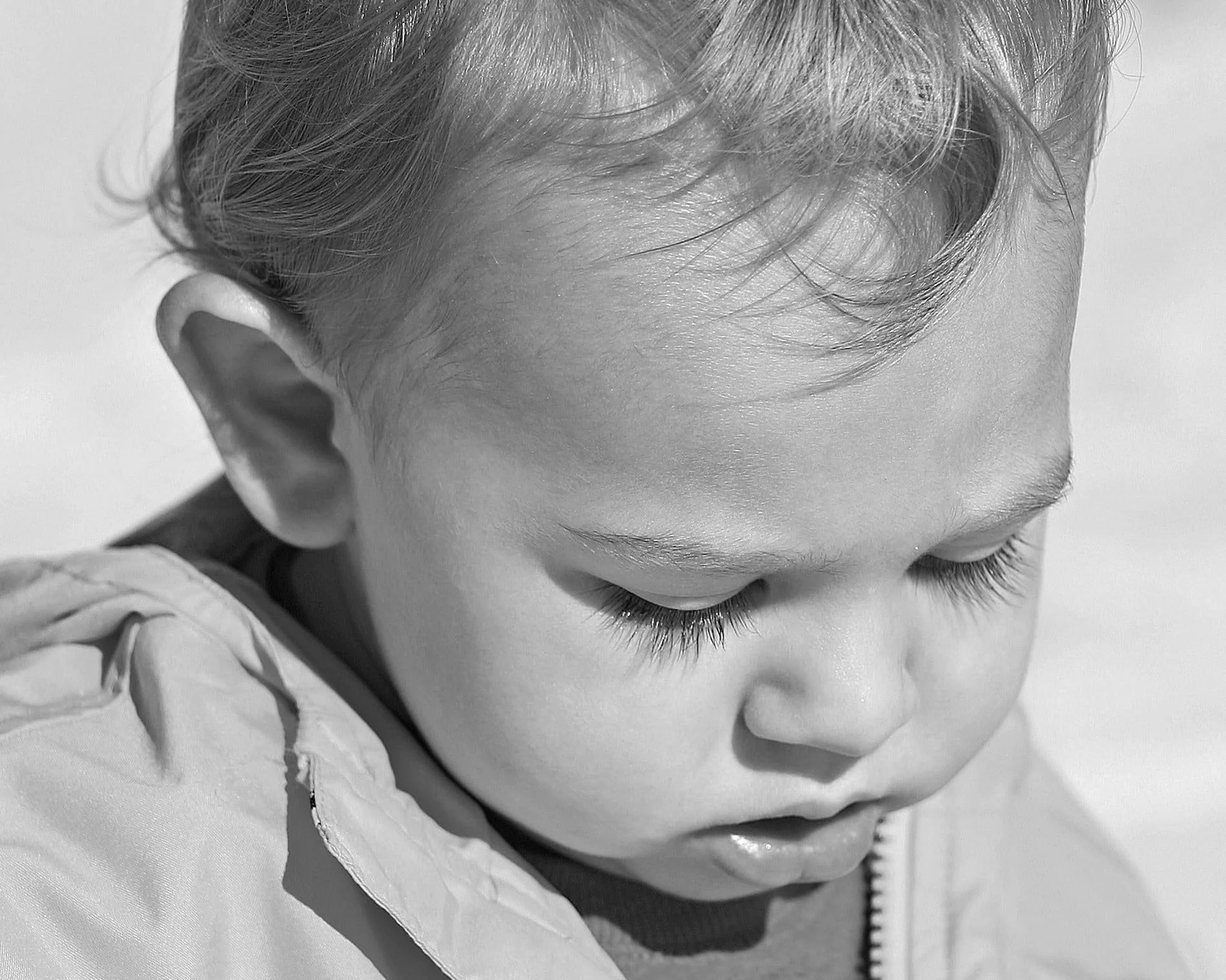 Close-up black and white photo of a young child with closed eyes, dark eyelashes, and light hair, wearing a light-colored jacket, exploring Perdido Beach.