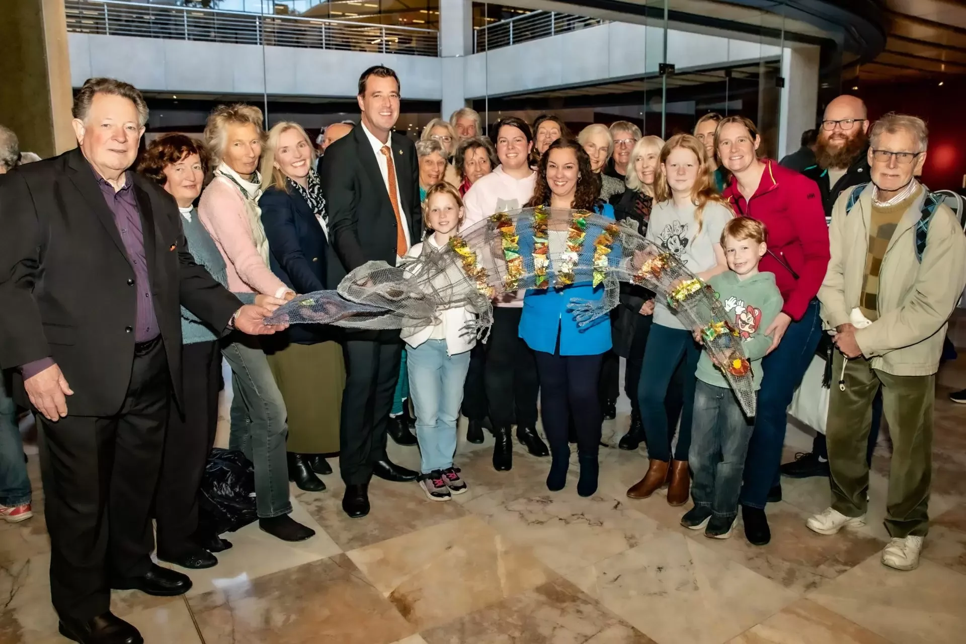 Group of adults and children posing indoors with a large decorated net sculpture