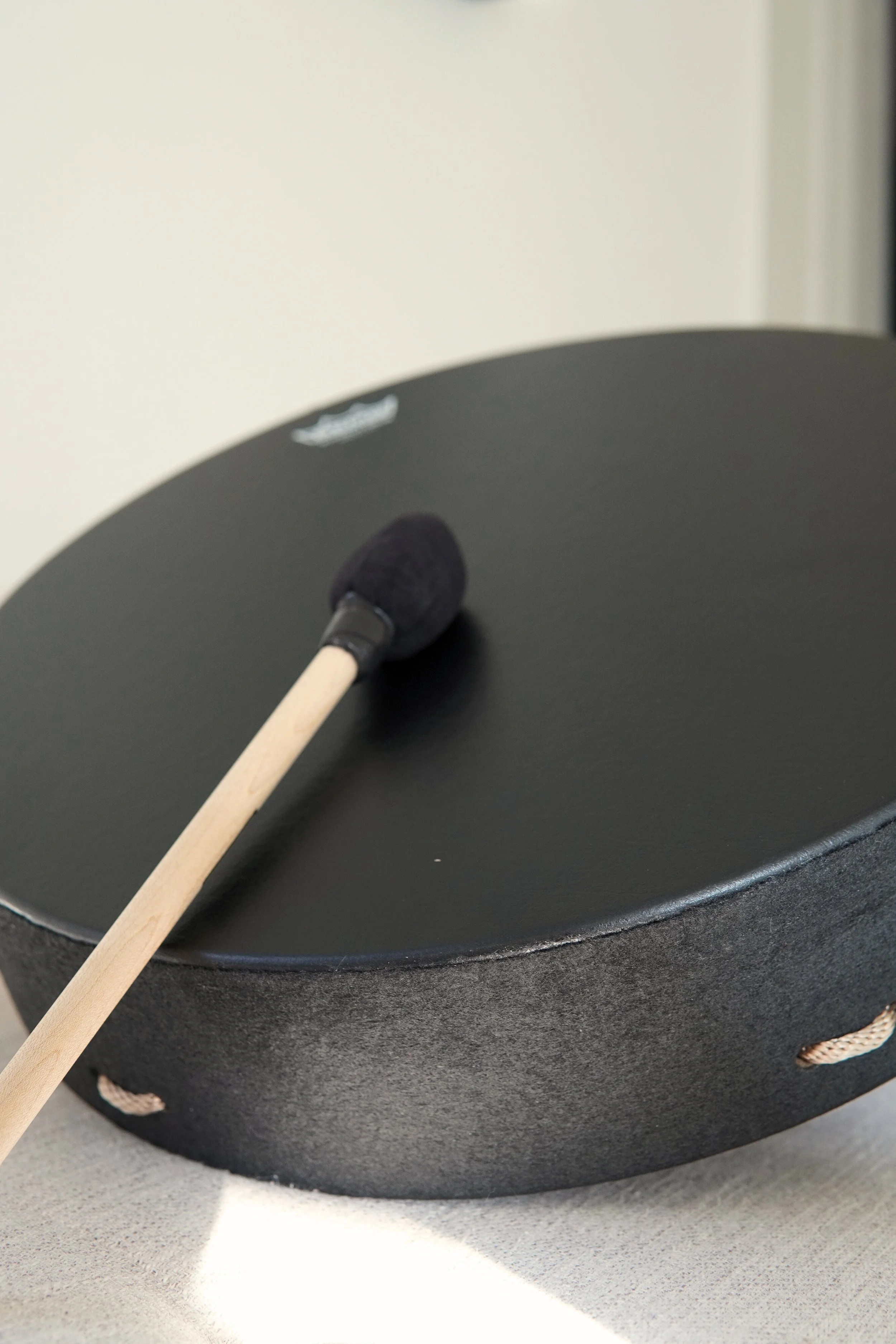 A black musical gong with a mallet resting on top, placed on a neutral surface.