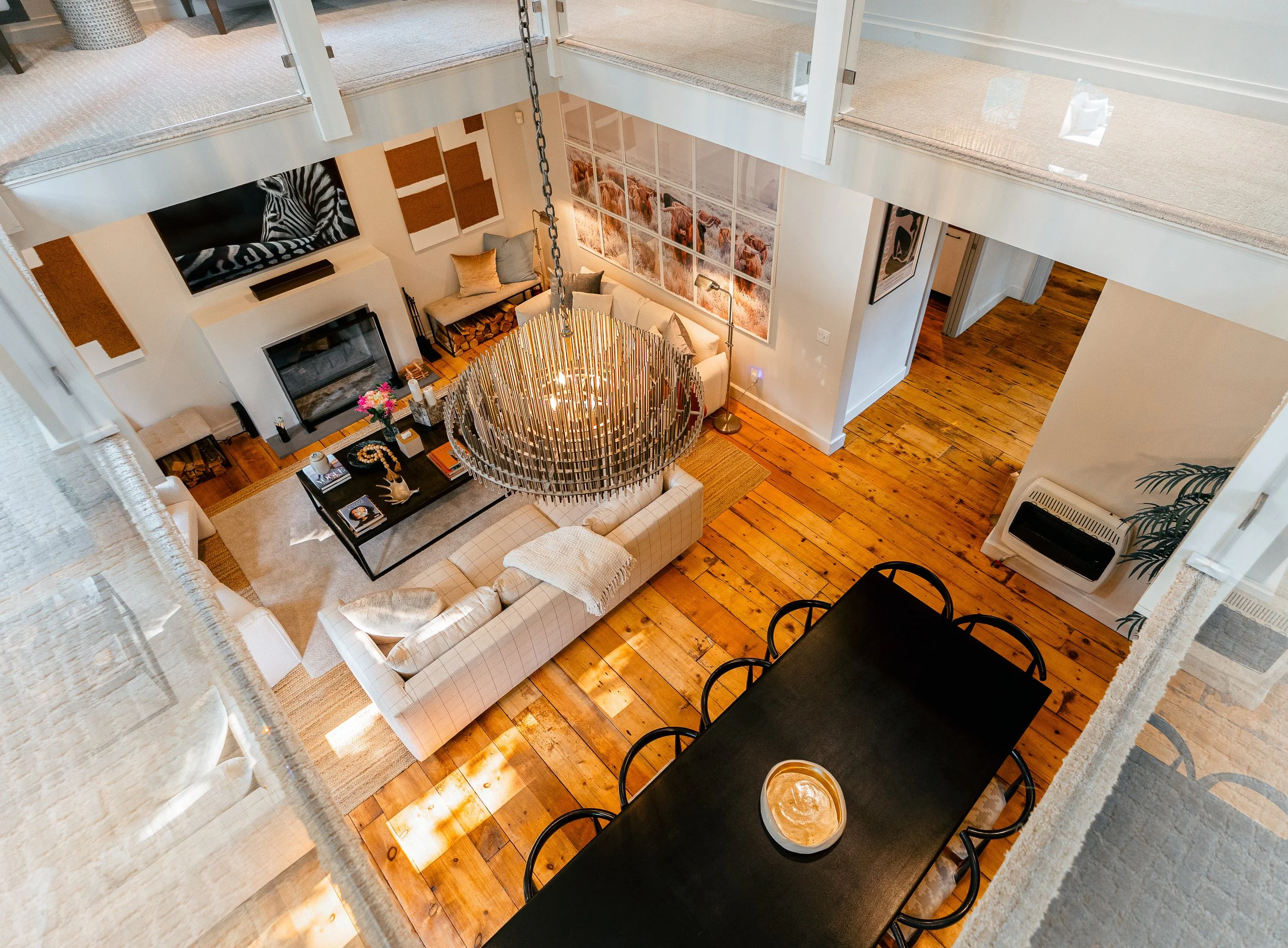 Open-concept living and dining area with hardwood floors, modern furniture, a large chandelier, fireplace, and decorative wall art.