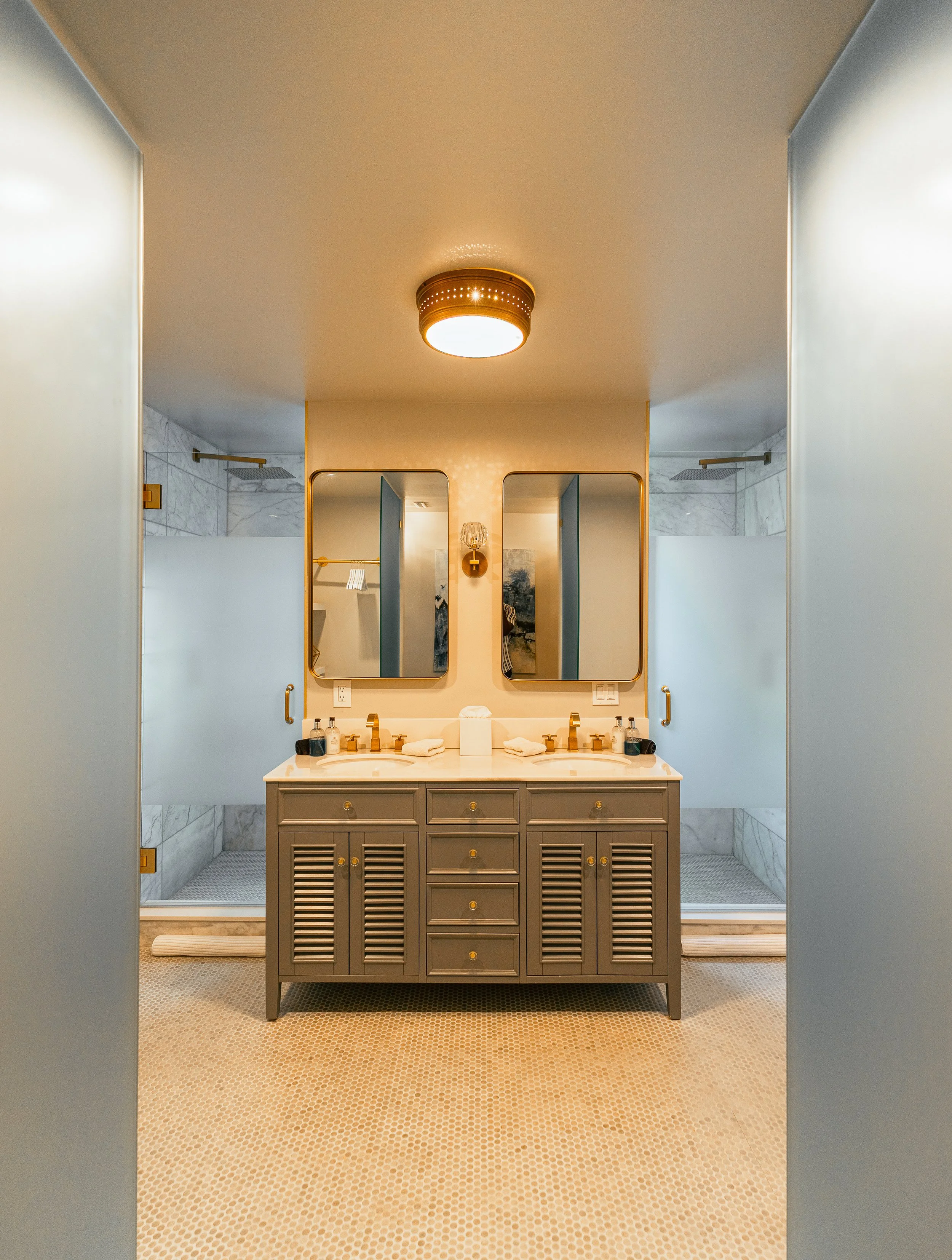 A bathroom with a double vanity, two mirrors, and two private shower stalls with frosted glass doors.