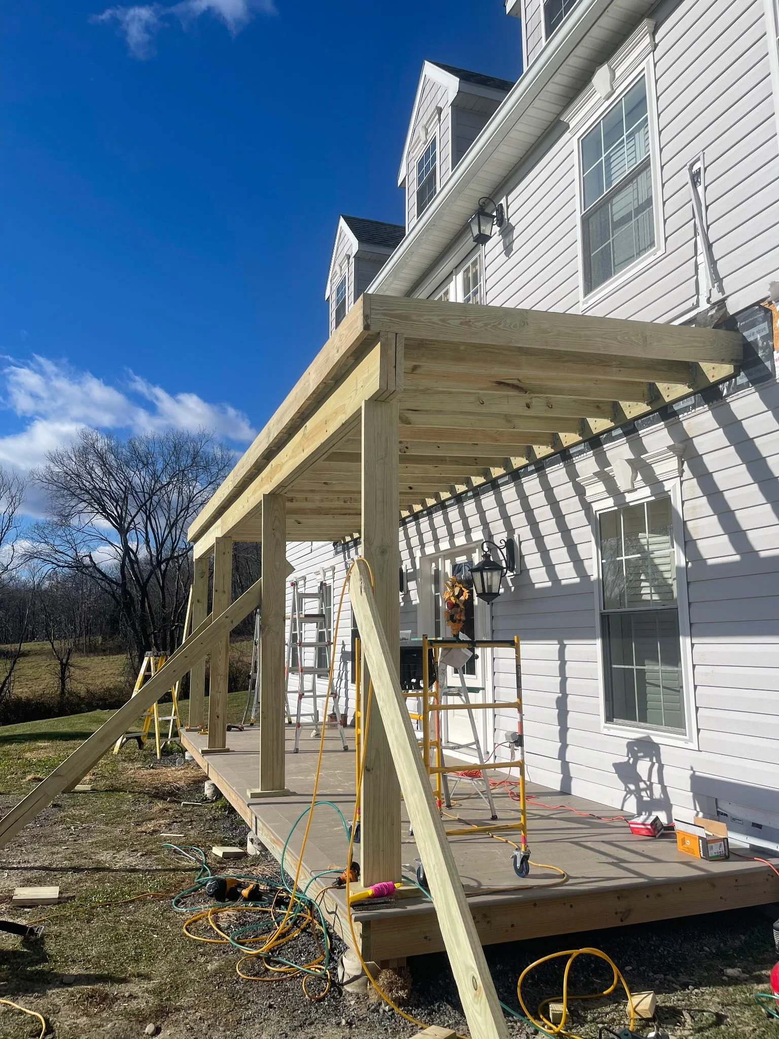 Construction of a wooden deck attached to a white house under sunny skies.