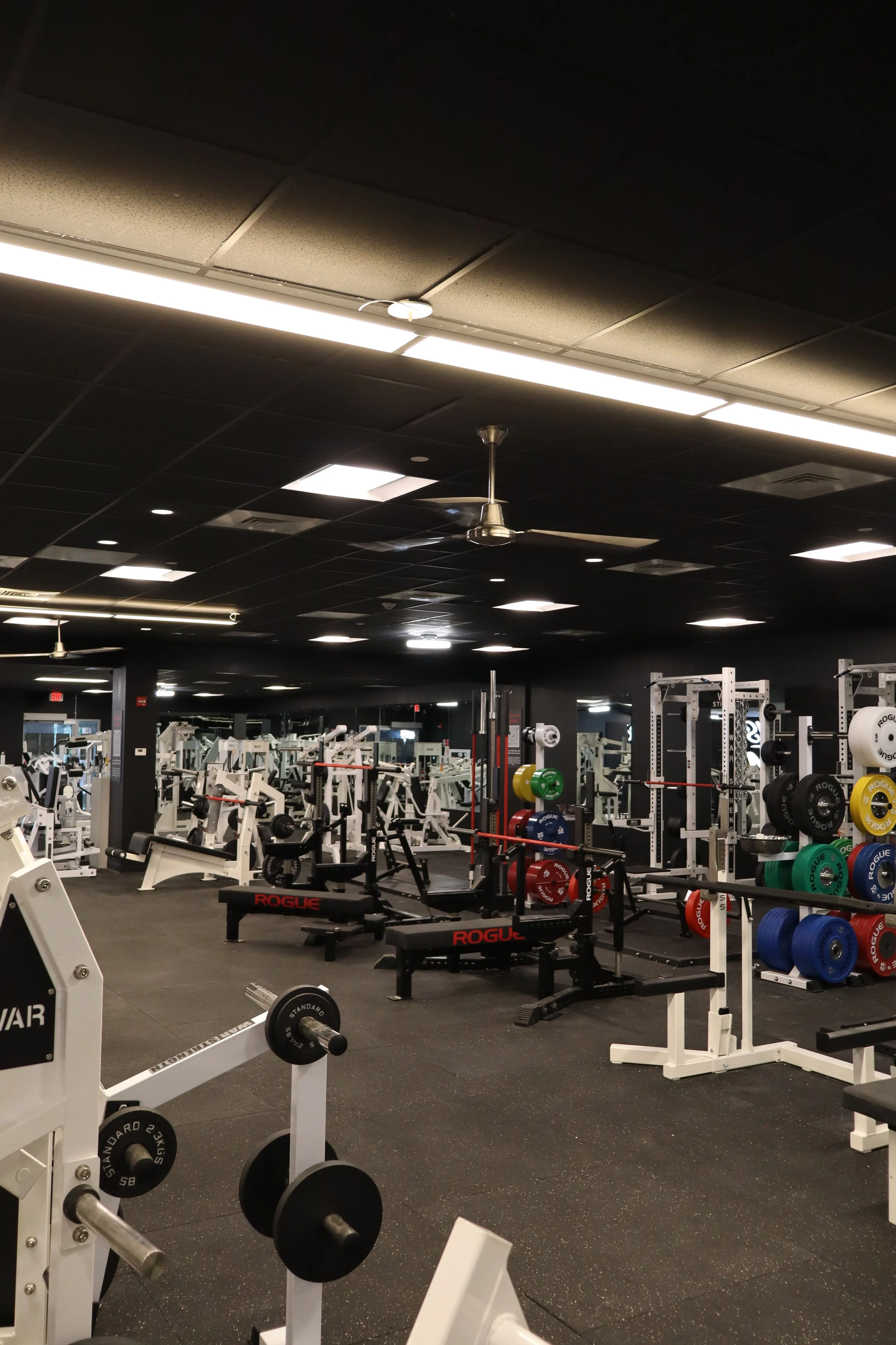 Empty gym with weightlifting equipment, benches, and barbells in a spacious workout area.
