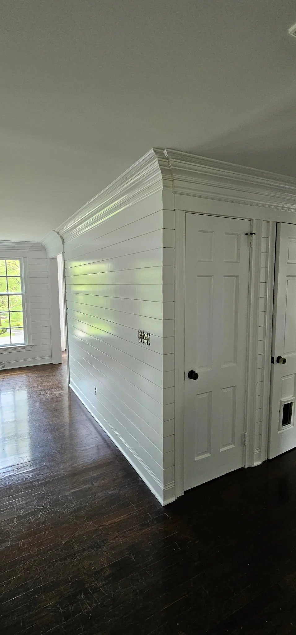 Interior of a house with white walls, dark hardwood floors, and large windows letting in natural light.