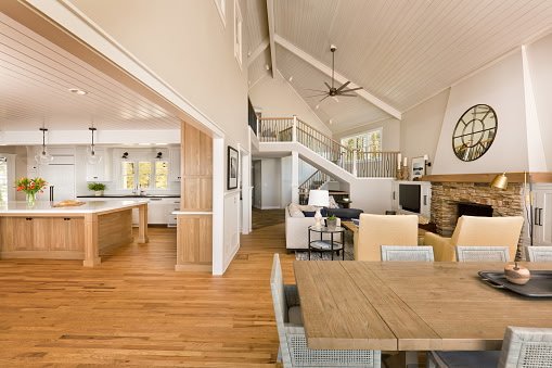 Open-concept living and dining area with high vaulted ceiling, fireplace, wooden floors, and modern decor.