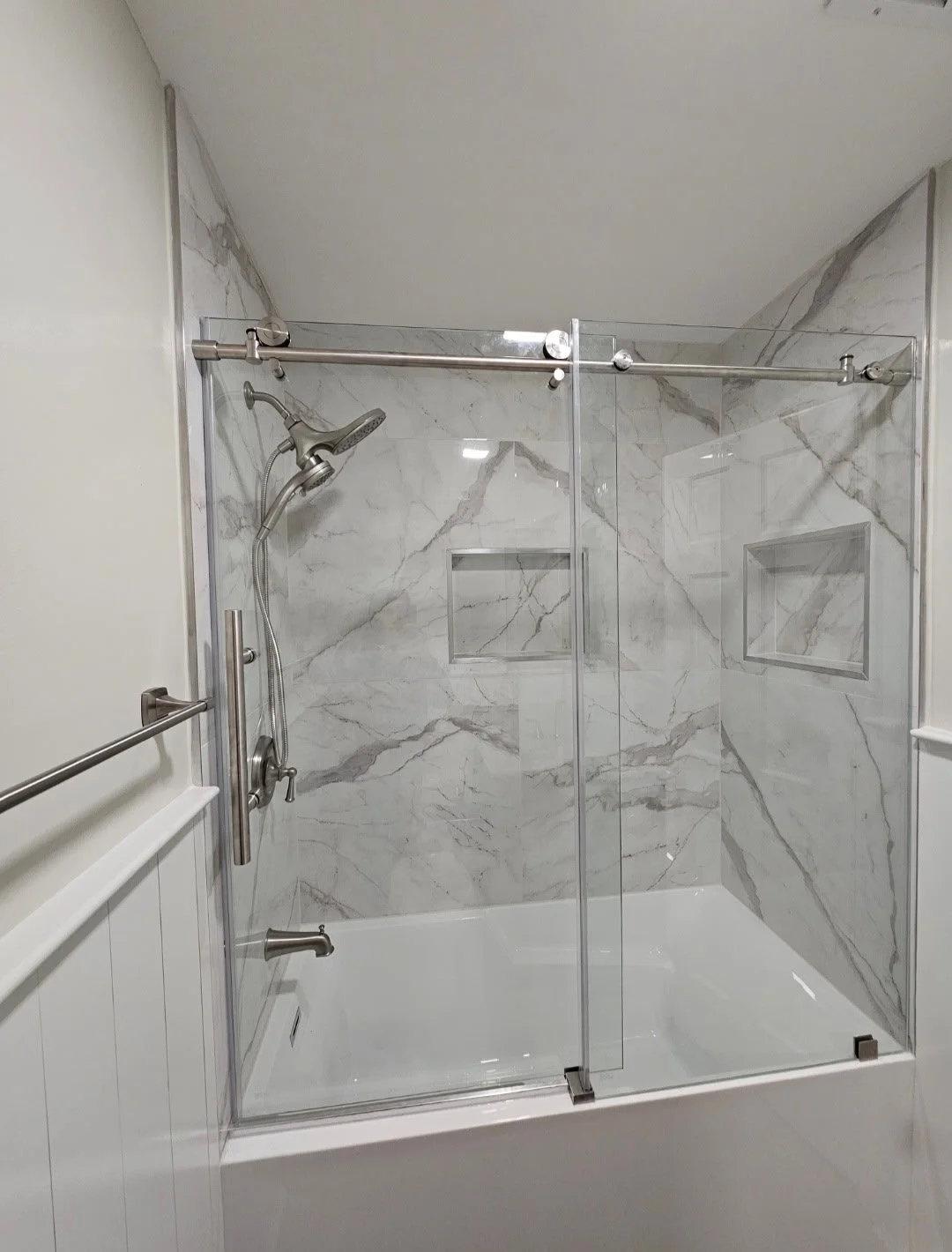 A modern shower with marble wall tiles, sliding glass doors, and built-in wall niches.