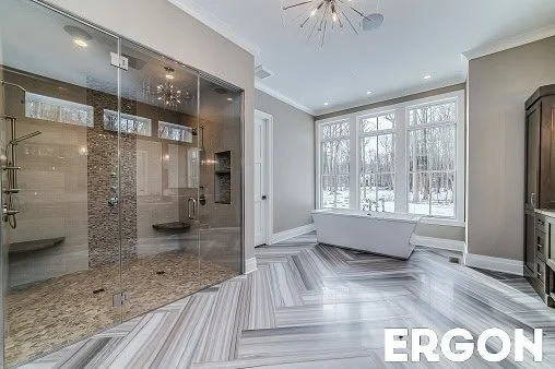Modern bright room with large windows, staircase, and free-standing bathtub, featuring a spacious glass shower enclosure with benches.