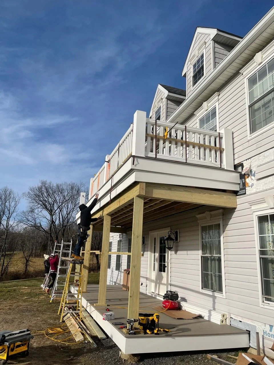 Construction workers building a wooden deck and porch under a balcony of a white house.