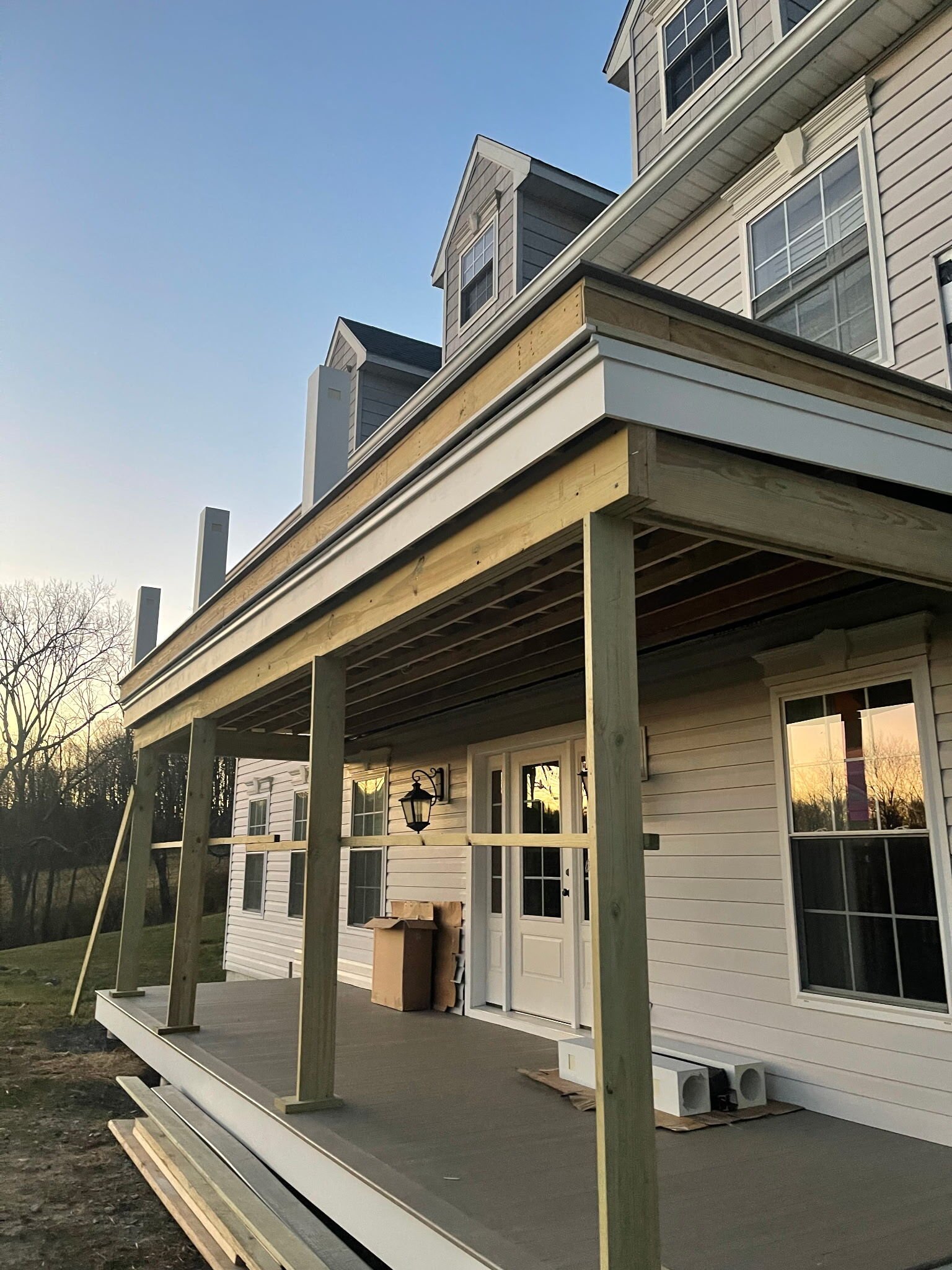 Construction of a wooden deck on the back of a white house with multiple windows and a door, during sunset.