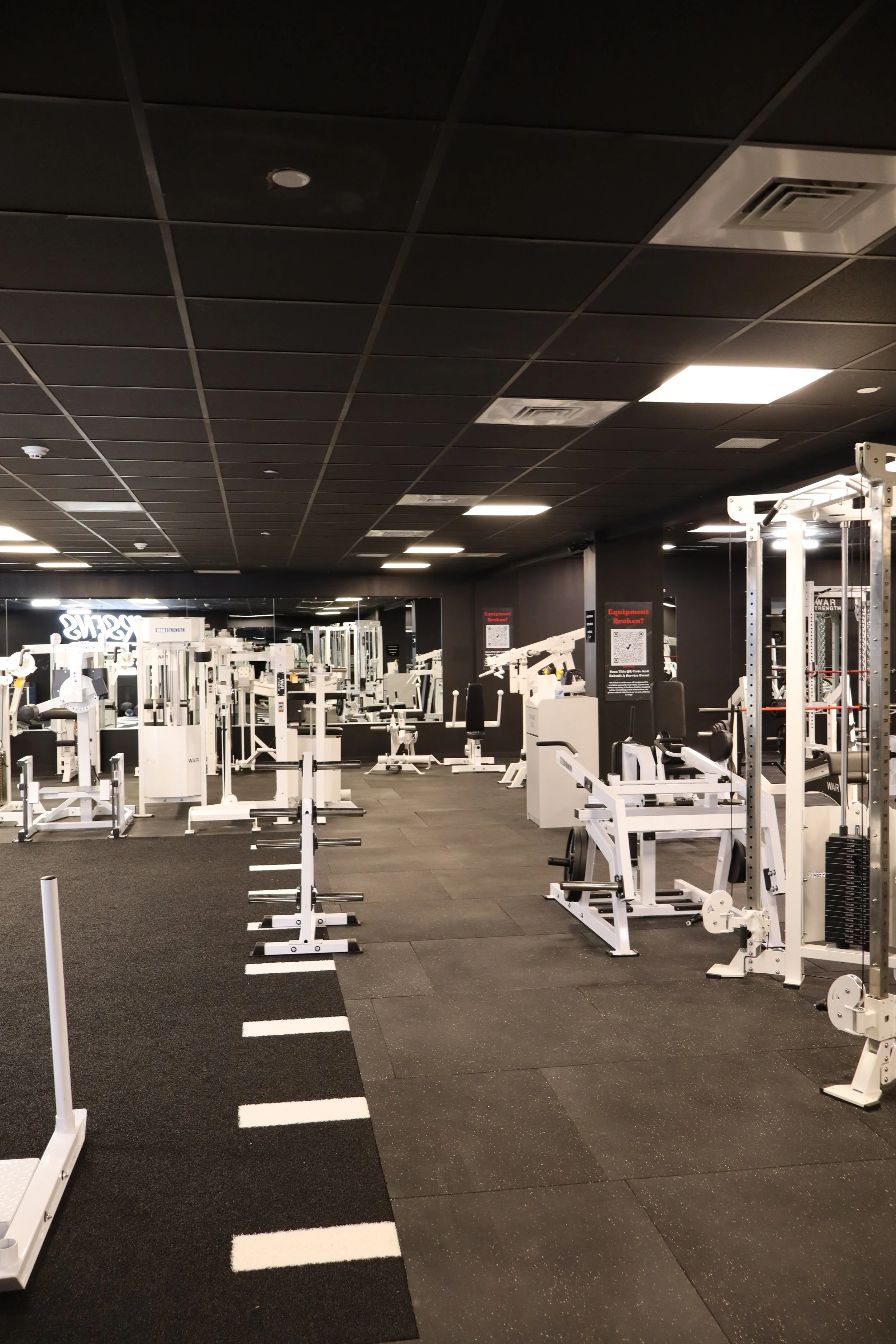Empty gym with various workout equipment and black ceiling.