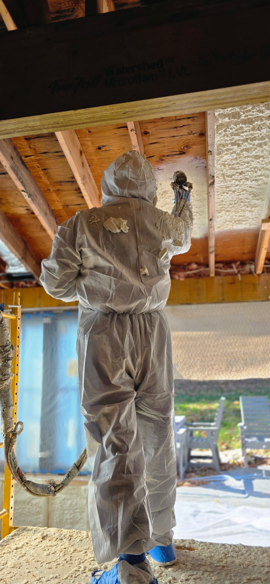 Person in protective suit spray-foaming ceiling of a building under construction or renovation.