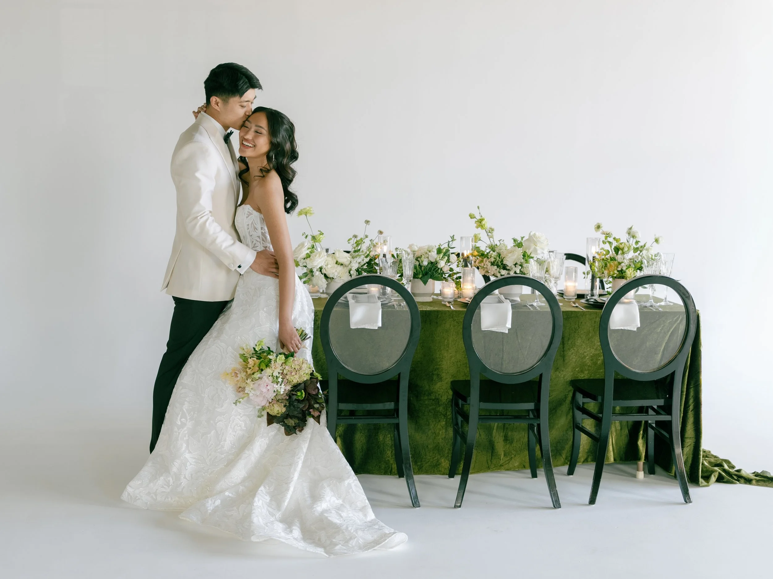 A newlywed couple embracing in front of a decorated wedding reception table with flowers and candles.