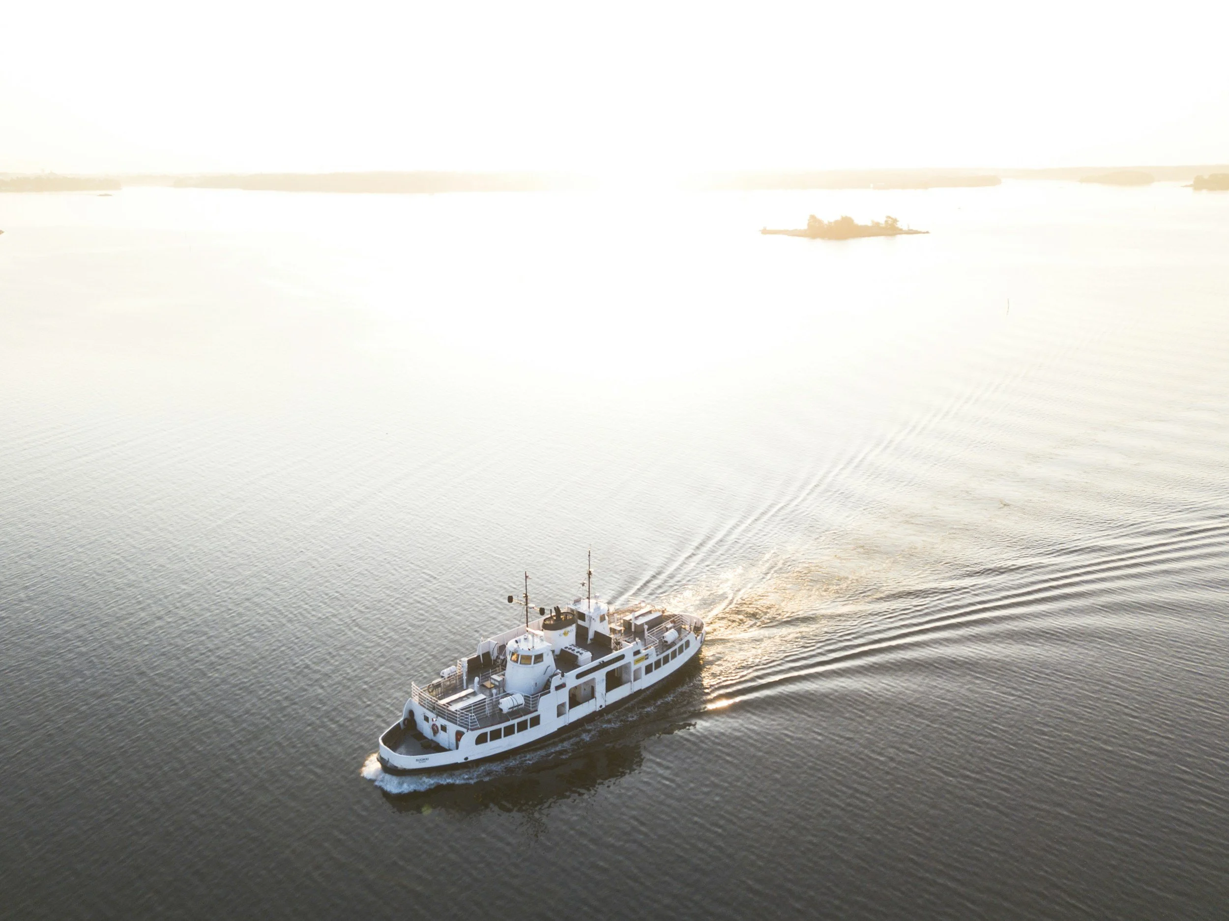 A white boat sailing on calm water during sunset with land in the background.