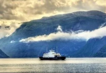 A ship sailing near a large mountain or glacier with foggy skies overhead.