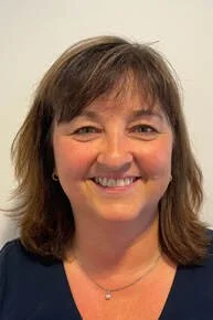 Smiling woman with shoulder-length brown hair, wearing a navy top, against a light background.