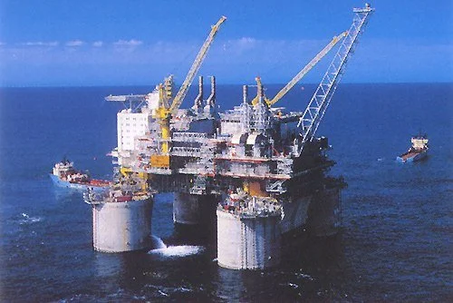 Offshore oil drilling platform with cranes and support vessels in the ocean.