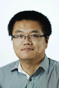 Portrait of an Asian man with short black hair, wearing glasses and a light blue collared shirt, neutral expression, white background.