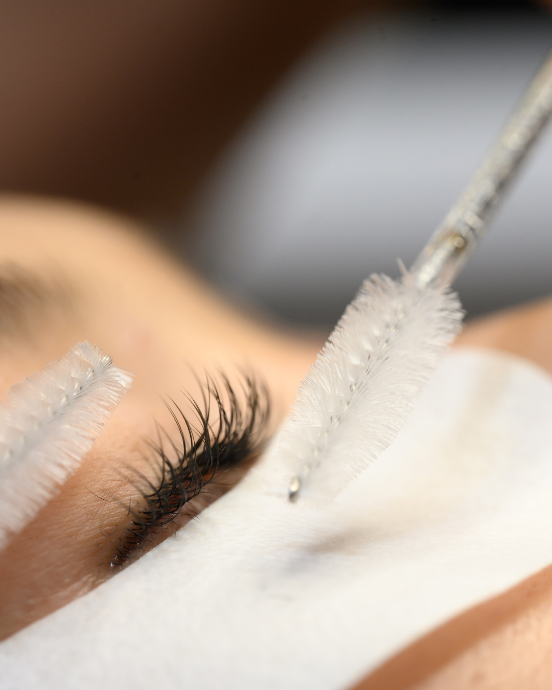 Close-up of a person receiving or undergoing an eyelash extension process with a wand applicator and cleaning swabs nearby.