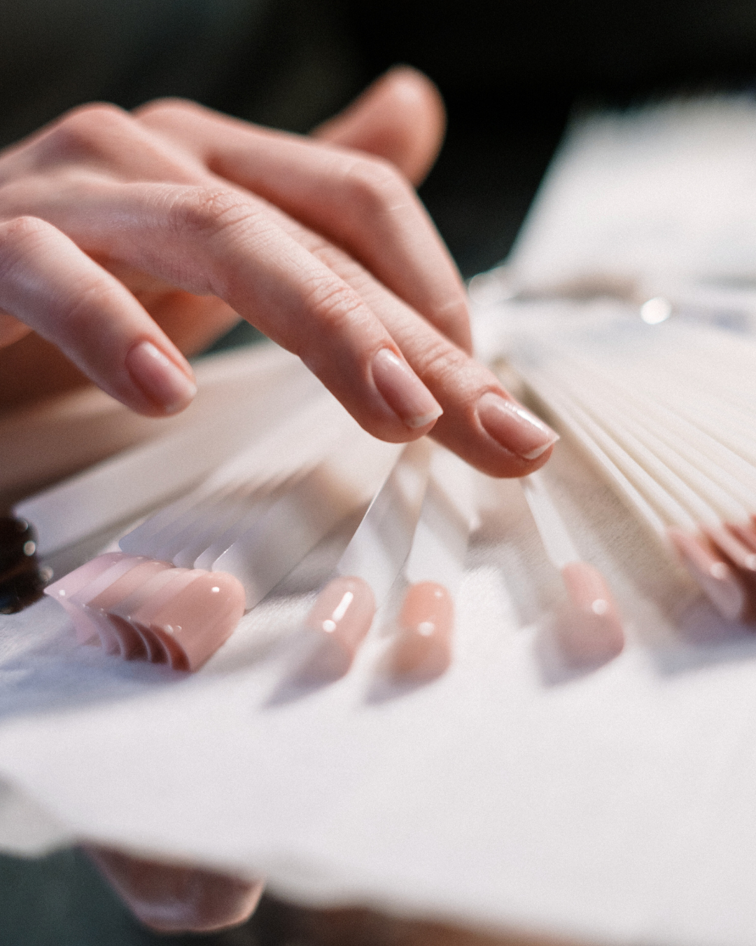 A person's hand flipping through nail polish color swatches in a salon setting.