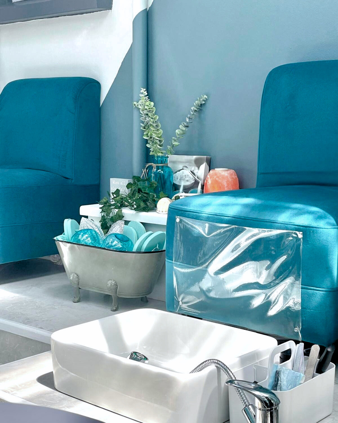 Salon station with teal chairs, a white sink, a small side table with decorative plants, vases, and a bowl of teal and blue items.