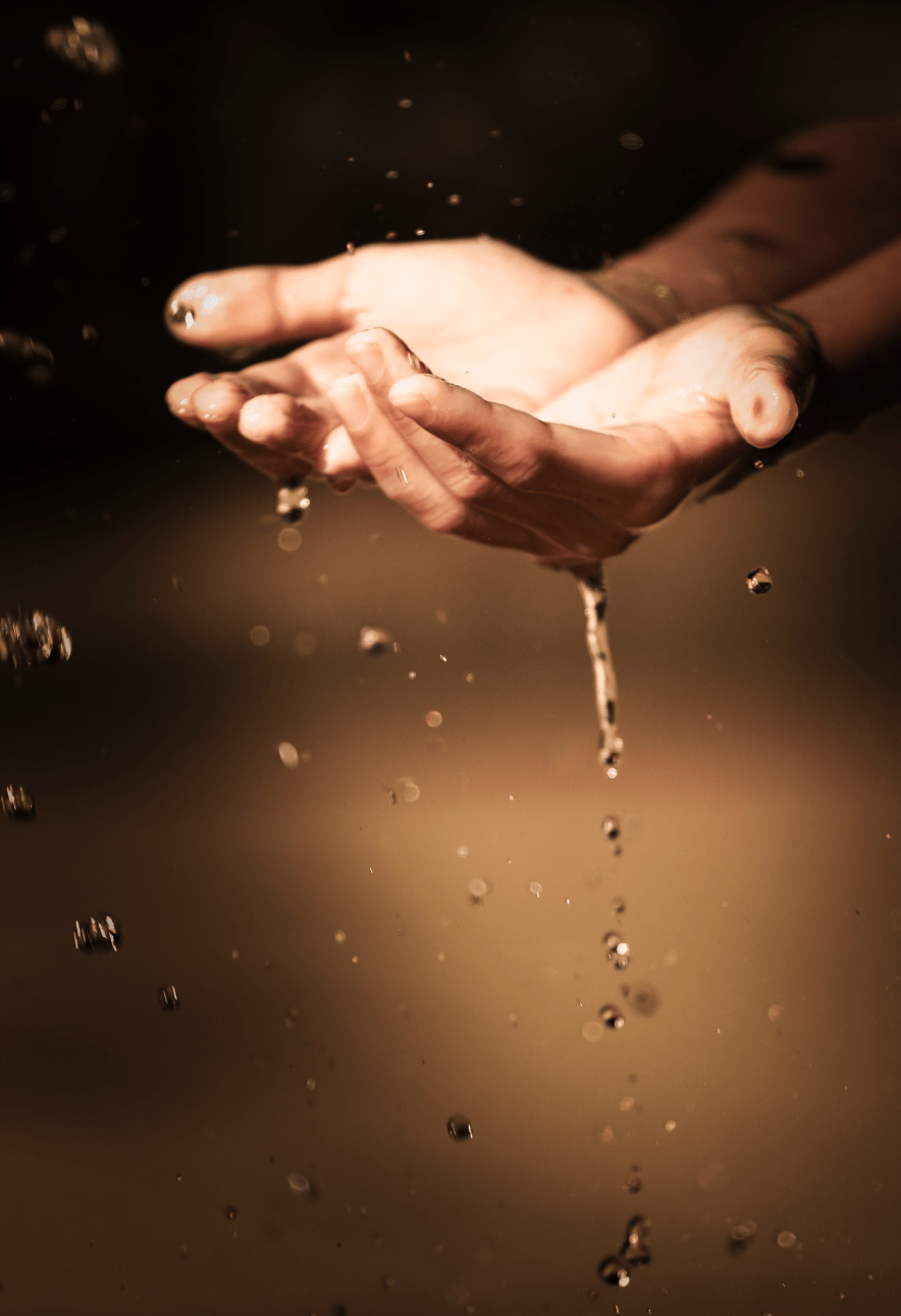 A pair of hands holding water, with droplets falling.