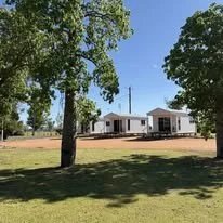 A house under construction with a clear blue sky, surrounded by trees, and a grassy lawn in the foreground.