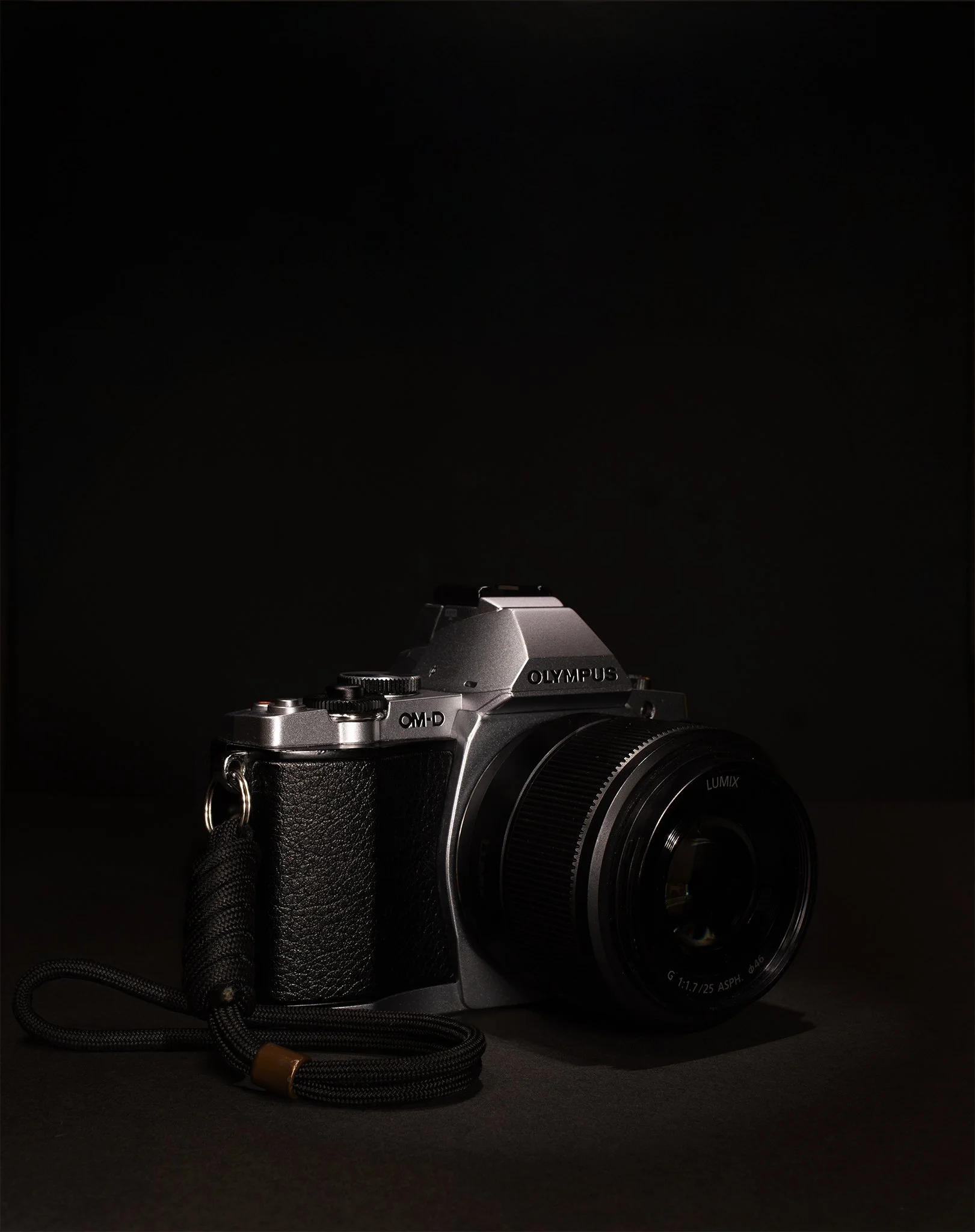 A silver and black Olympus camera with a attached lens, placed on a dark surface against a black background.