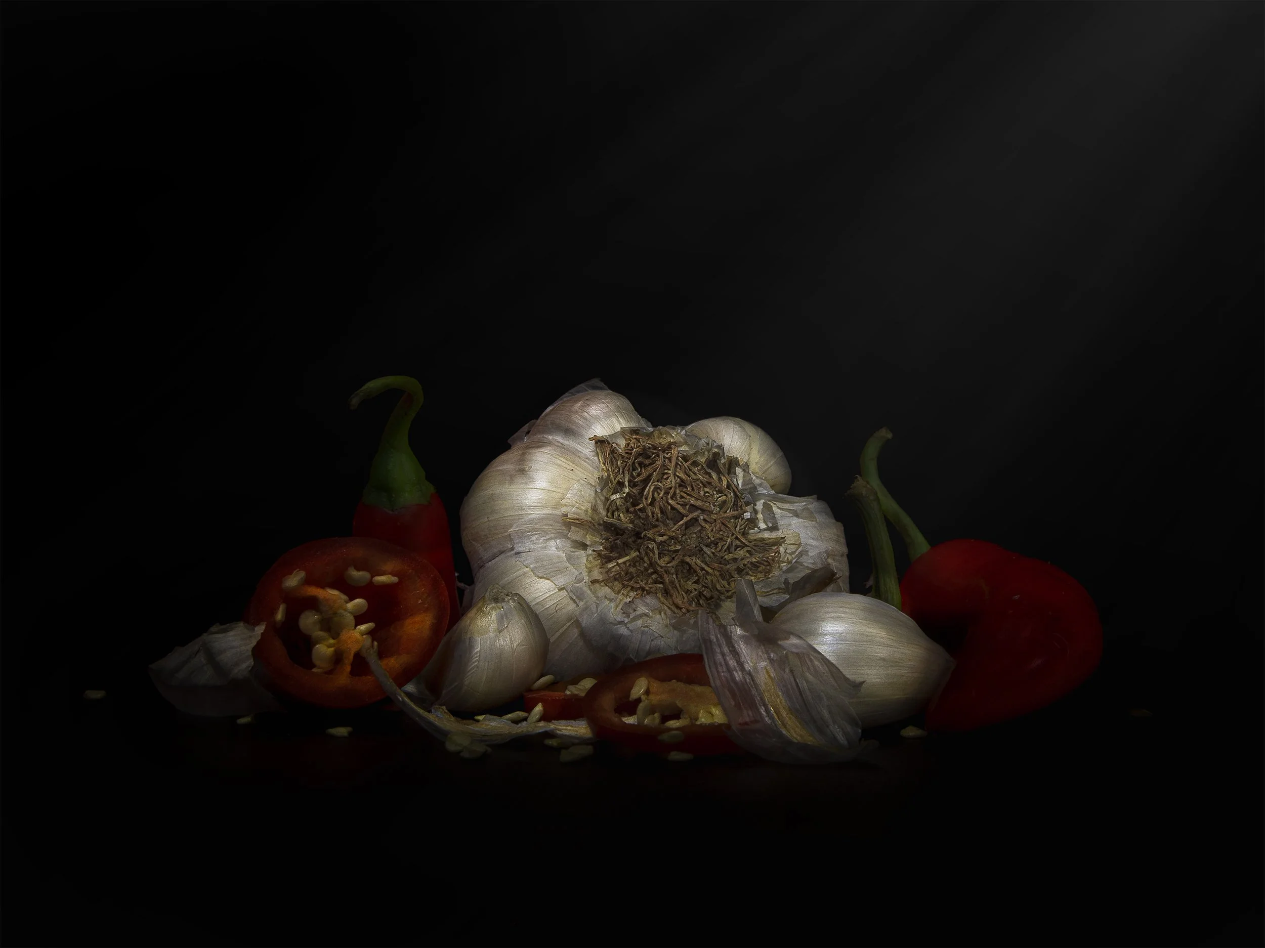 Garlic bulbs, red chili peppers, and chili pepper seeds scattered on a dark surface with a dark background.