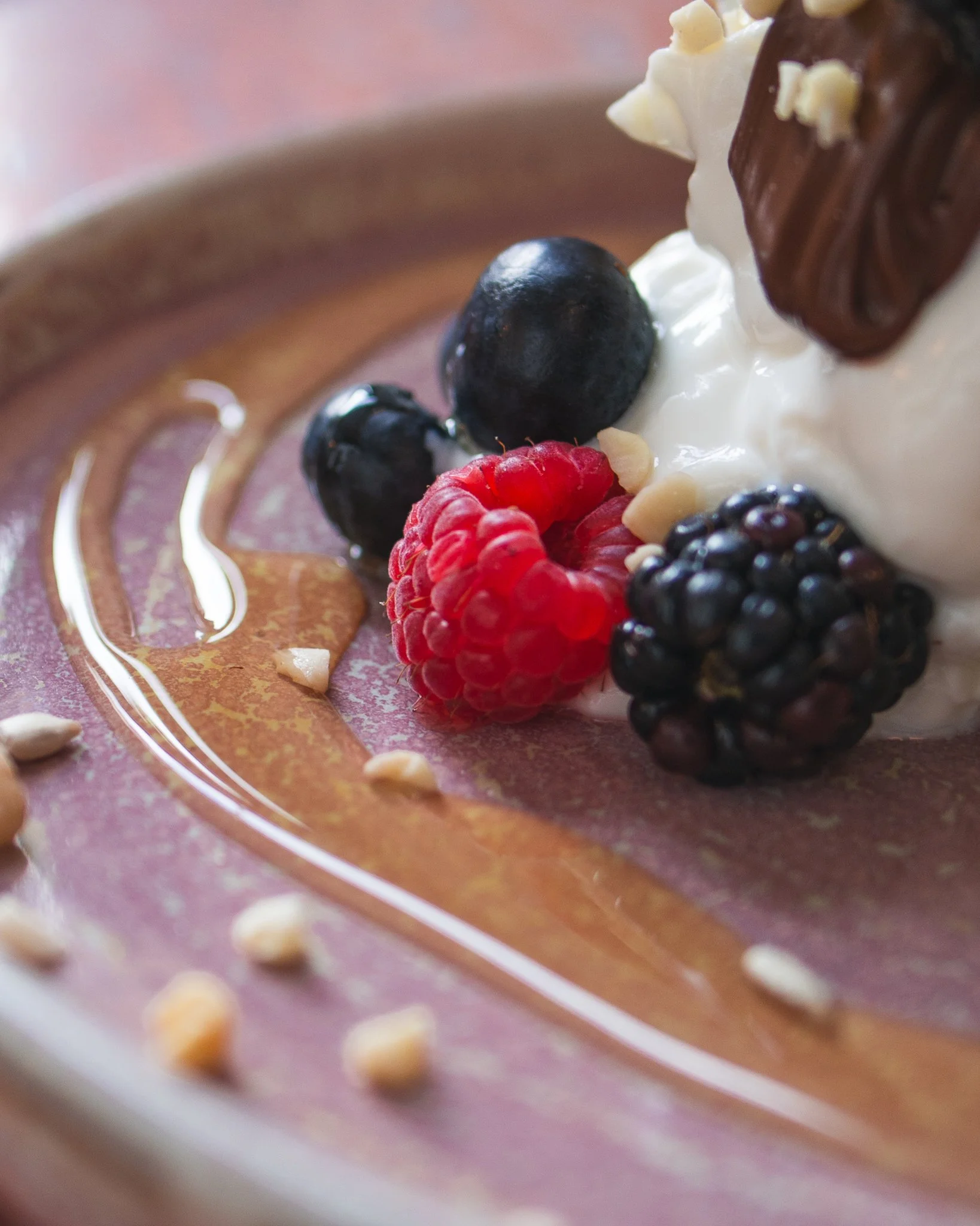 Close-up of desserts with berries, whipped cream, chocolate, and caramel sauce on a pink plate.