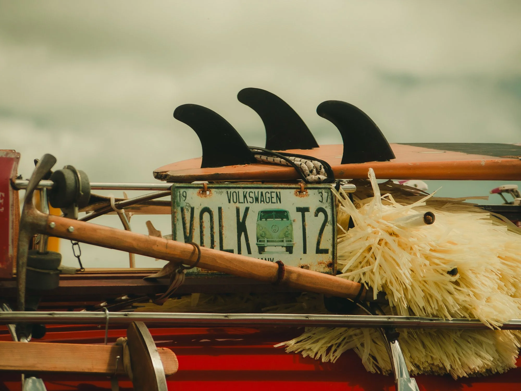 Surfboards with fins and a Volkswagen license plate attached to a cart, surrounded by a broom and other items.