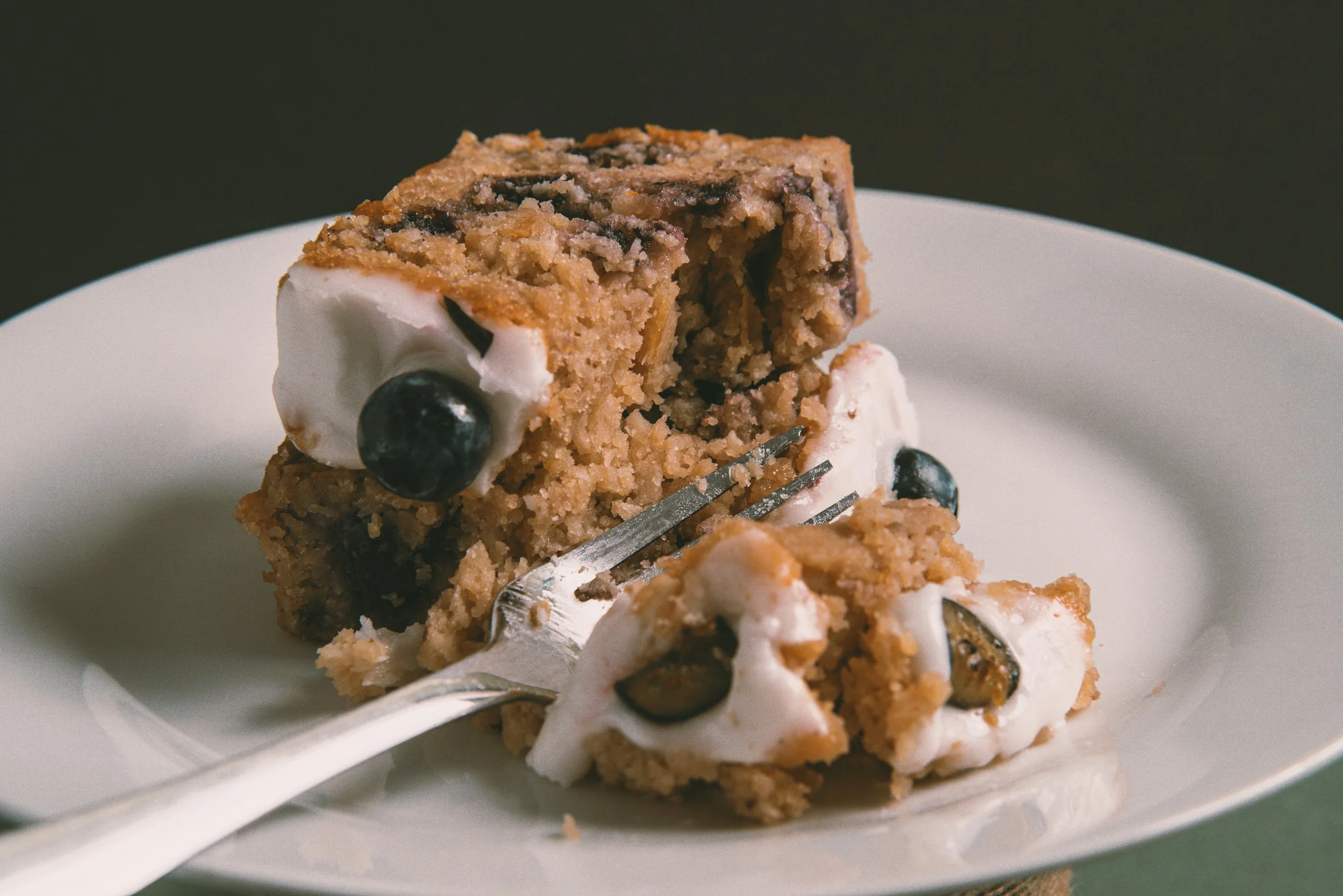 A close-up of a slice of blueberry crumble with whipped cream on a white plate.