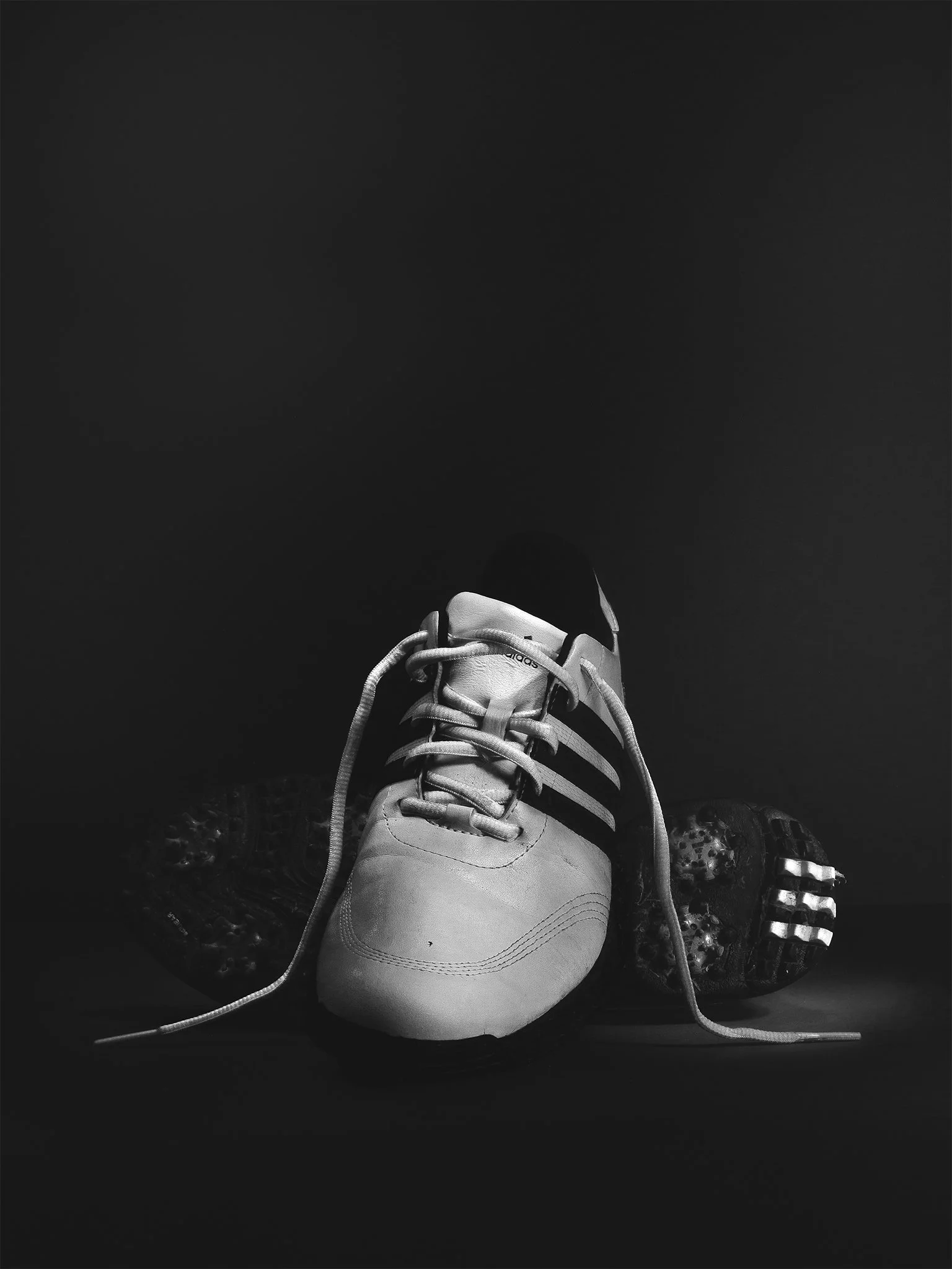 Black and white photo of a pair of athletic shoes, with one shoe upright and the other lying on its side, against a dark background.