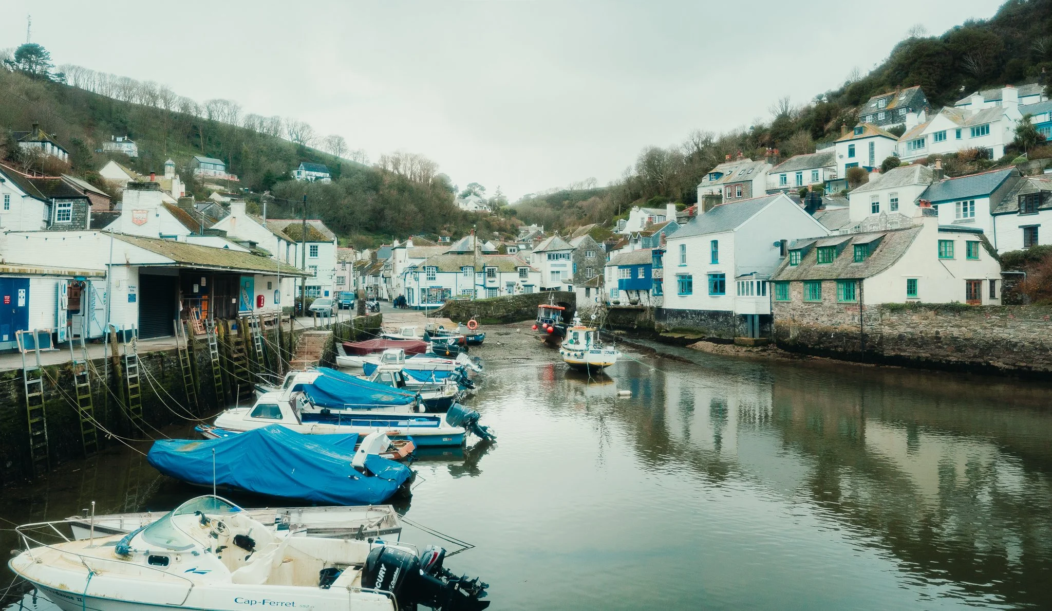 A harbor scene with small boats docked along the water, surrounded by white and colored houses on a hillside.
